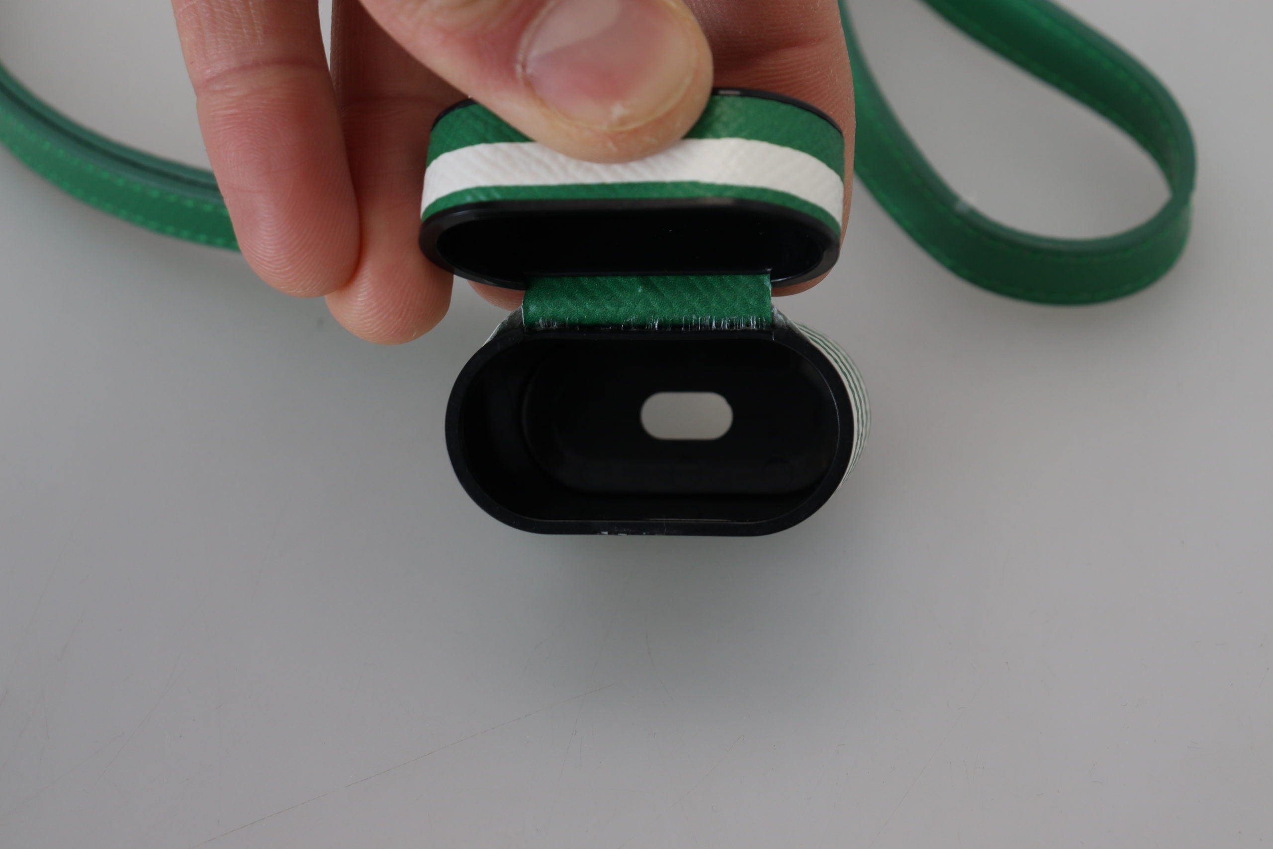 Pouzdro na Airpods se zeleným koženým řemínkem a zlatým kovovým logem
